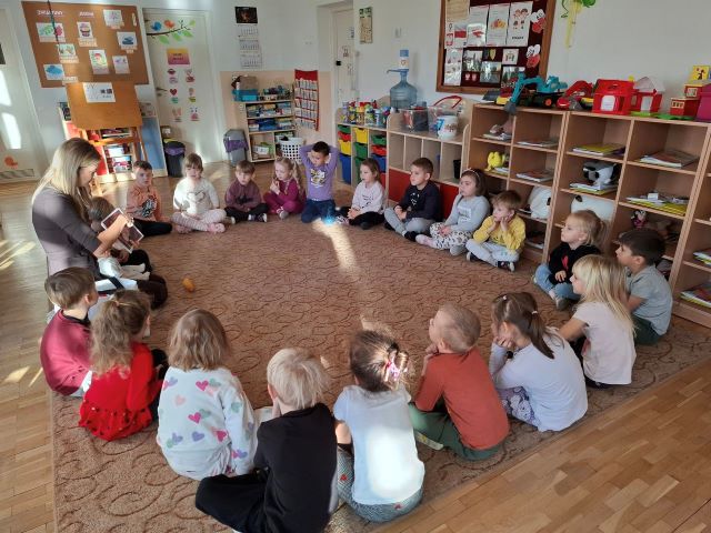 dzieci siedza na dywanie i sluchaja czytania przez mame